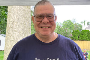 Man in blue tee shirt wearing glasses smiling at camera on a summer day