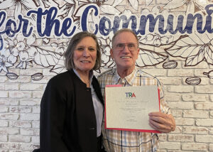 Smiling woman standing at left next to happy man who has received a certificate of thanks for volunteering