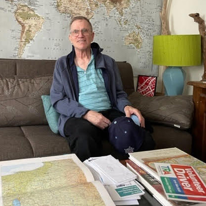 Man relaxed and sitting couch with maps on wall in background and foreground