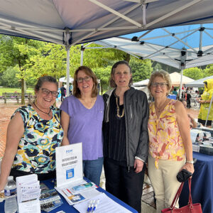 Group of four woman standing under tent and near sign FSW interested in volunteering?