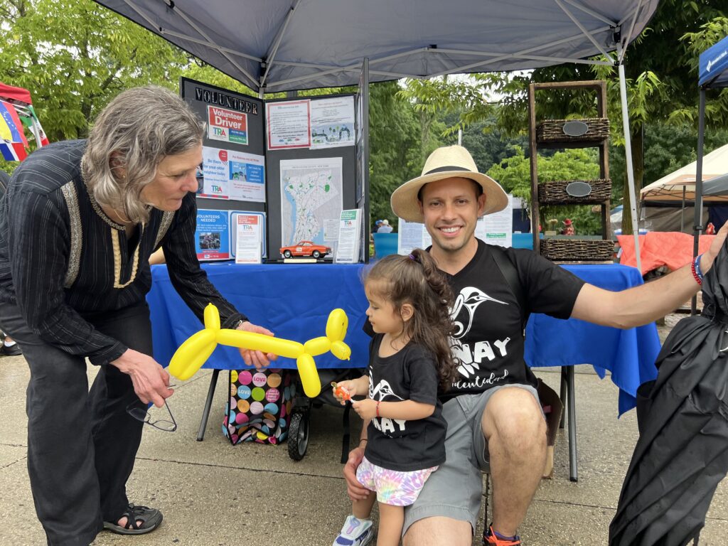 Young man with straw hat with his daughter in matching tee shirts and woman bending down to girl with balloon animal