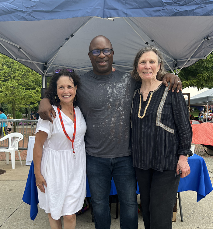 A diverse group of two women wit a man in between standing together under a tent