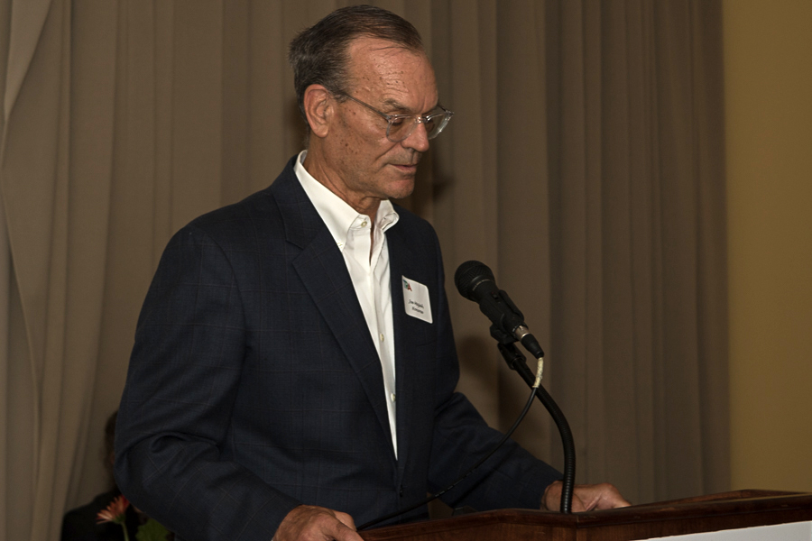 man in black suit jacket white button down shirt speaks at podium