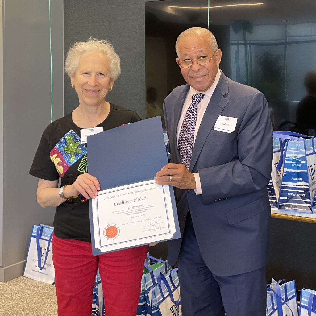 Volunteer in black t shirt and red pants smiles as Legislator Boykin presents certificate of merit
