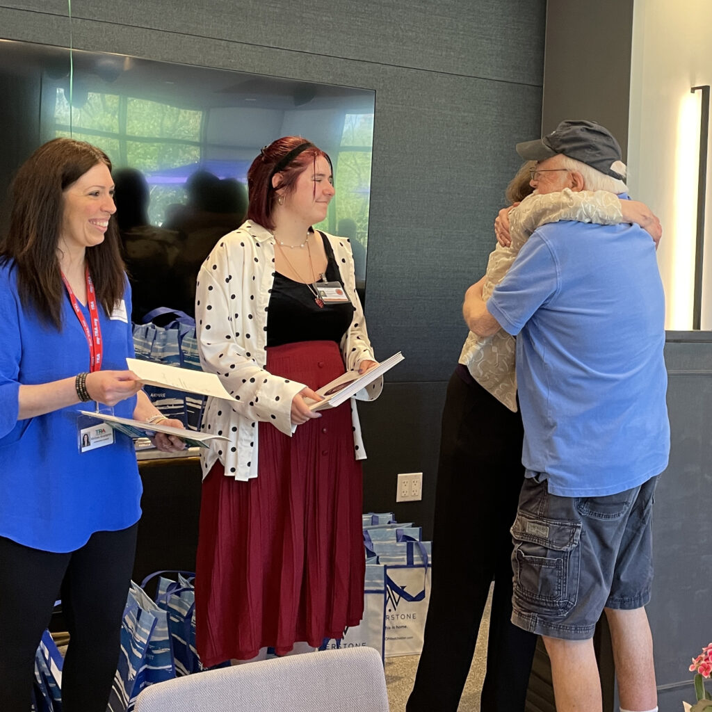 volunteer driver hugs TRA president while two women smile and look at them