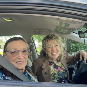 two women in front seat of car looking out ride side window and smiling