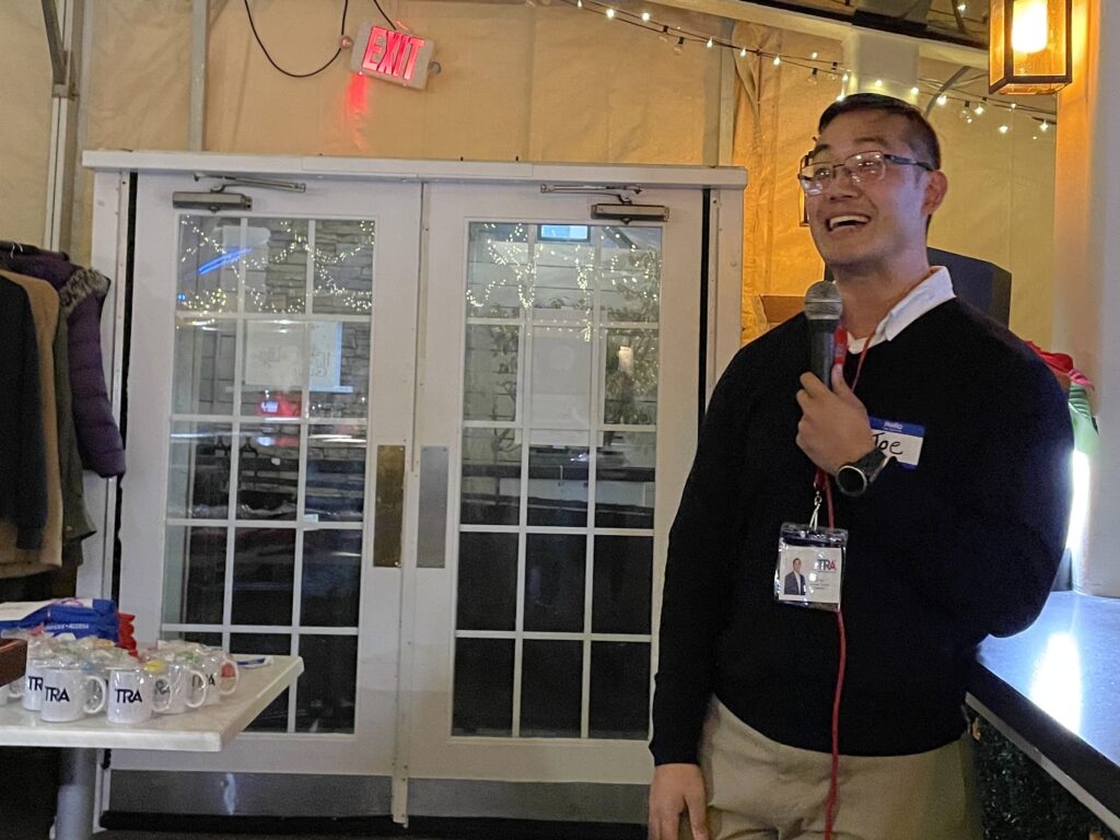 Man wearing glasses, holds microphone and smiles broadly