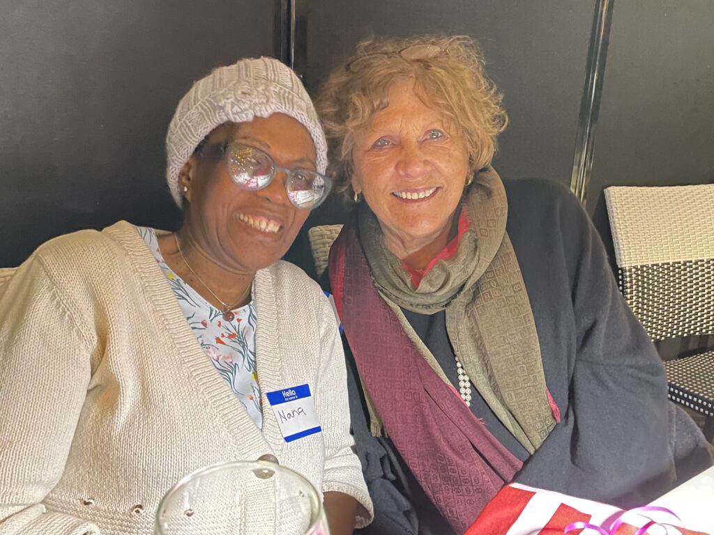 Two women seated, smiling, leaning toward each other