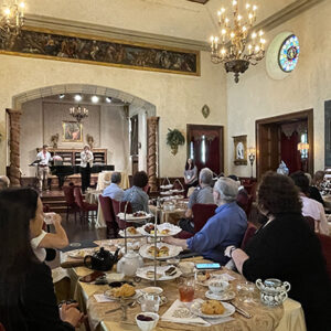square overview of elegant room hosting afternoon tea event with guests, set tables and view to stage