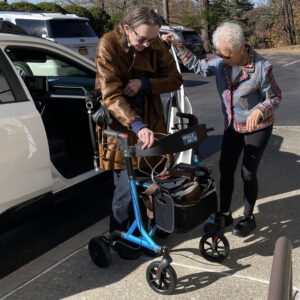 Woman assisting a second woman getting out of a car and using a walker