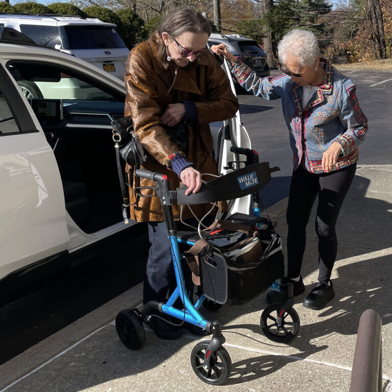 Woman assisting a second woman getting out of a car and using a walker