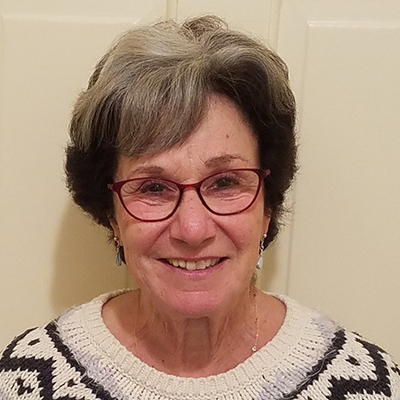 head shot of smiling woman with grey and black hair wearing glases