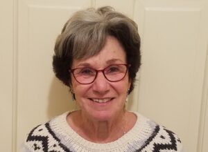 headshot of smiling woman with grey hair and Red eyeglasses