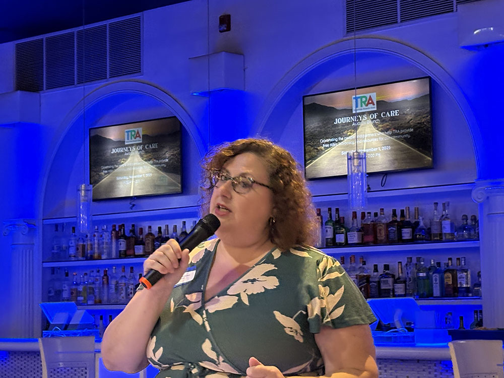 Close up shot of
Woman in dark green dress with floral print addresses people from the podium