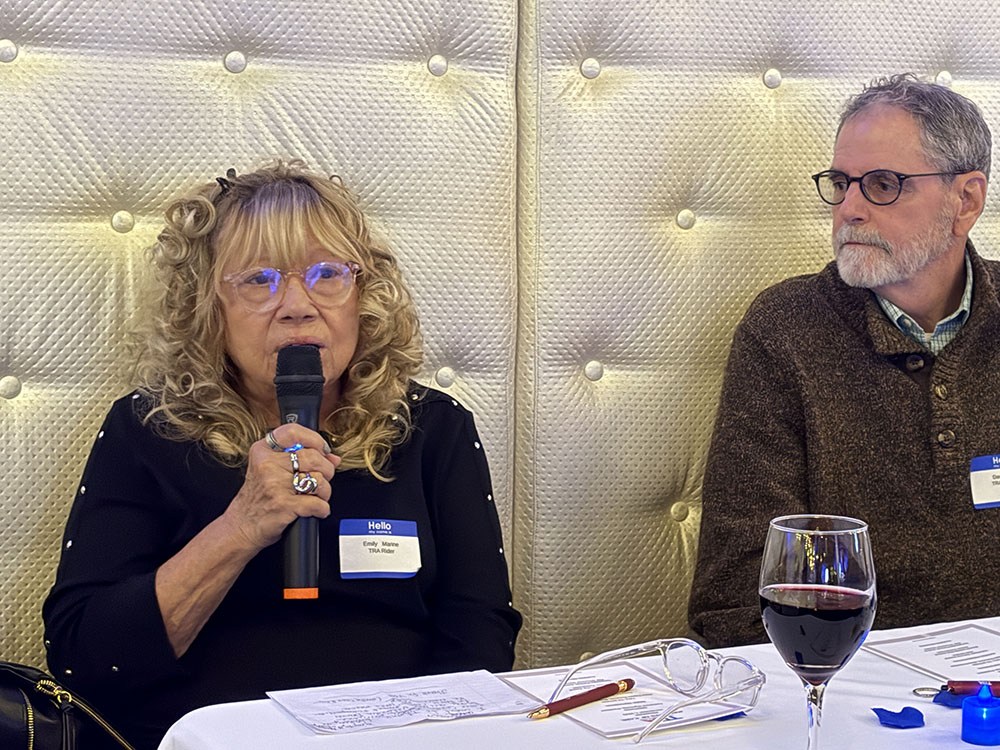 seated woman with blond curls speaks using a microphone