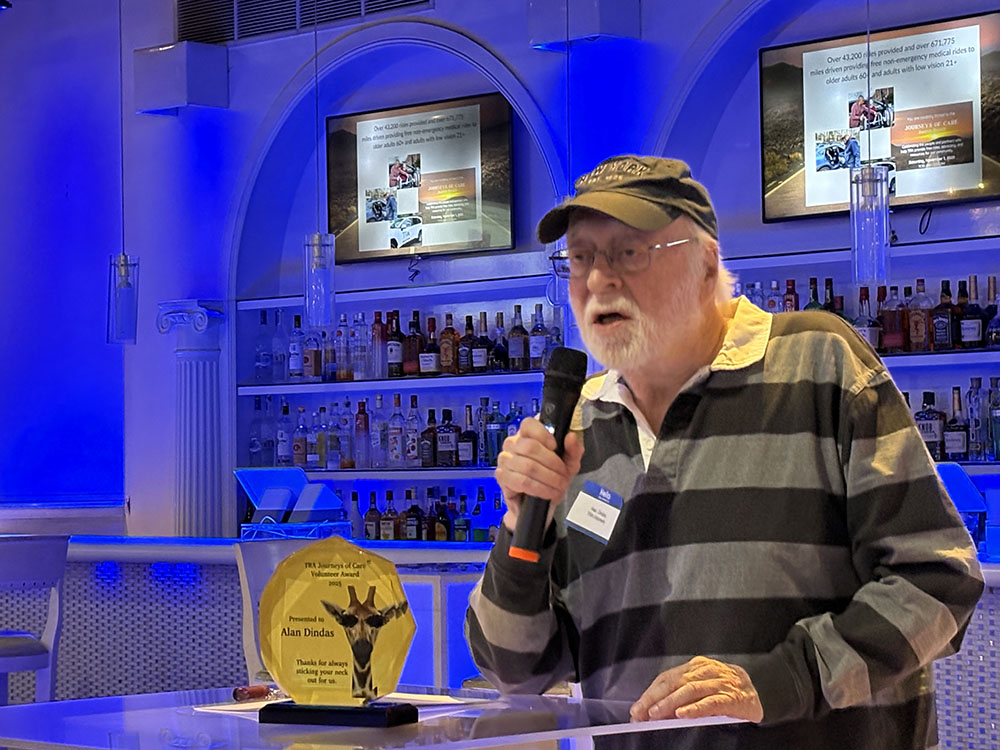 Awardee wearing striped shirt and baseball style hat speaks from the podium