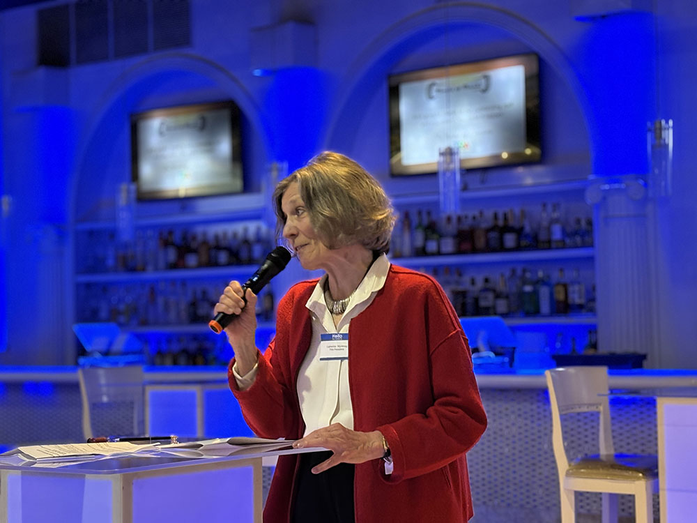 Woman wearing red sweater stands and speaks at pofium