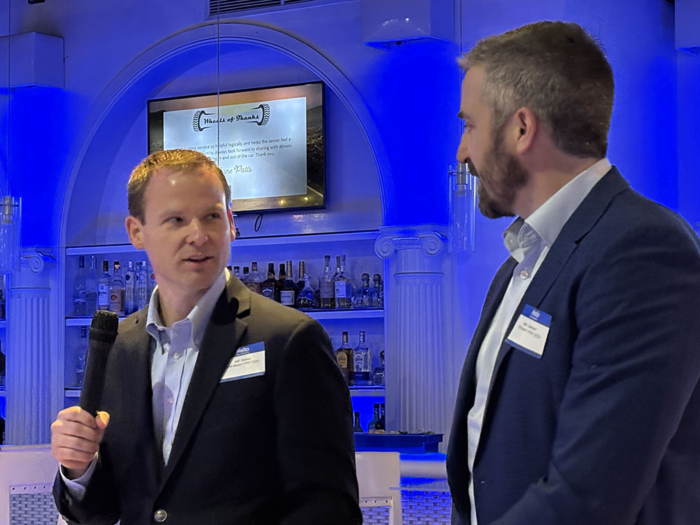 Two men standing at podium looking toward each other as one holds a microphone