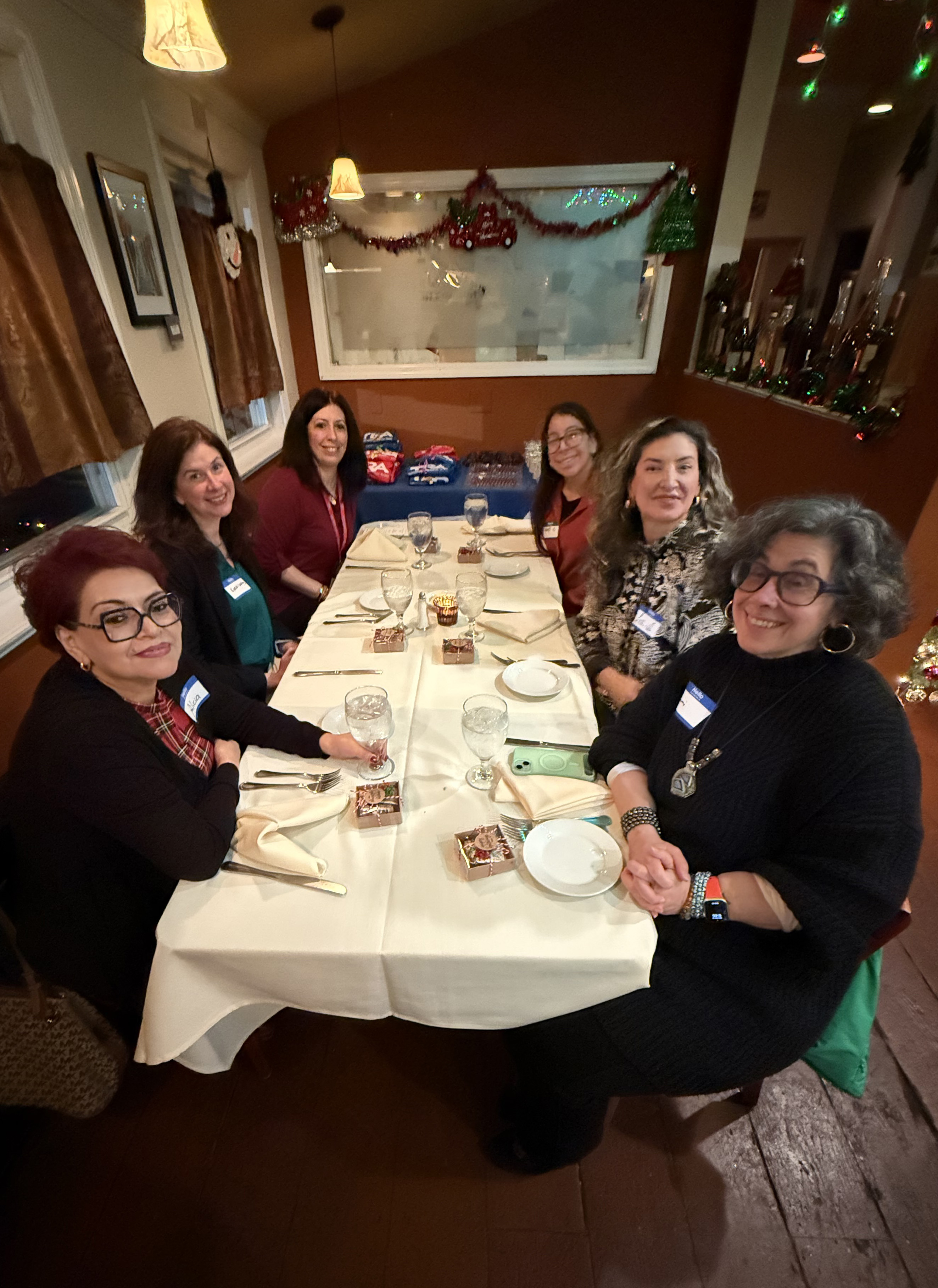 six women staff and volunteers sit at rectangular table with festive decorations volunteer winter luncheon