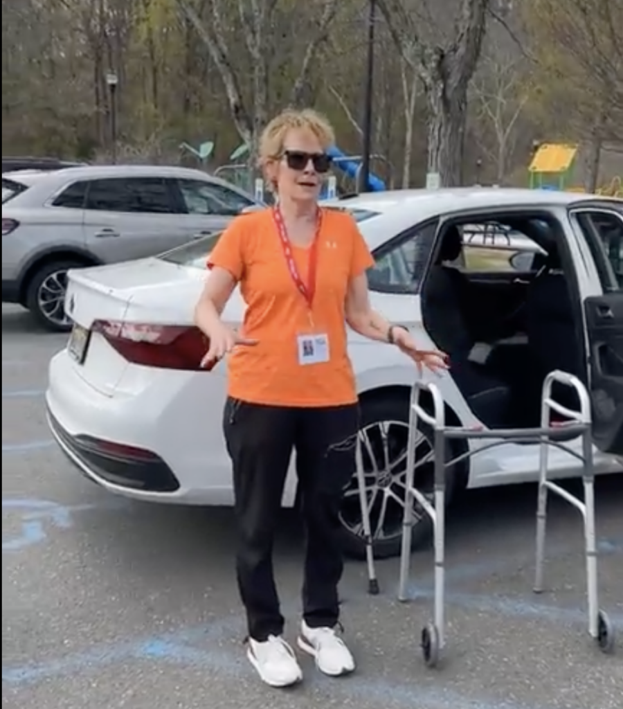 TRA training session on assisting riders into the car Woman in orange tee and sunglasses stands next to a walker and train as speaks
